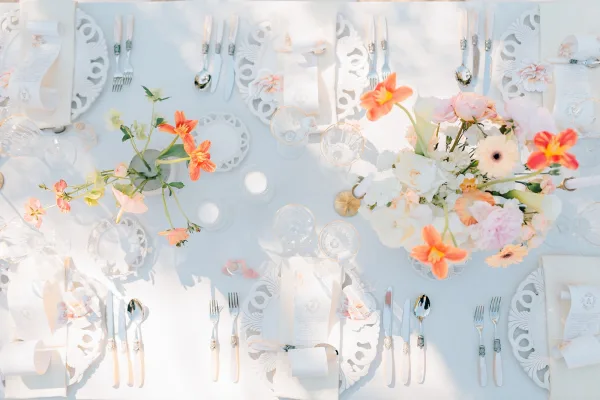 Reception tablescape with a wedding table setting on a white tablecloth, pastel floral centerpieces, menus, place cards, and candlelight in sunlight shadows