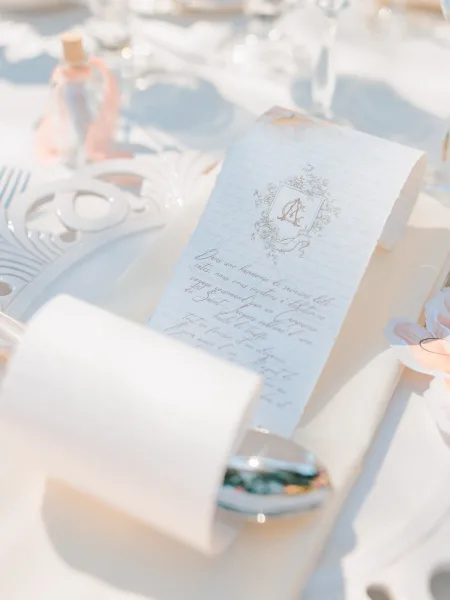 Wedding menu card with calligraphy wedding menu and monogram crest on deckle-edge paper at a place setting with silver flatware and candlelight