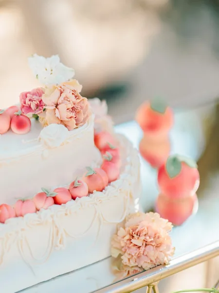 Wedding cake with peach themed wedding cake details, white buttercream piping, peach fondant and sugar flowers on a stand at reception table