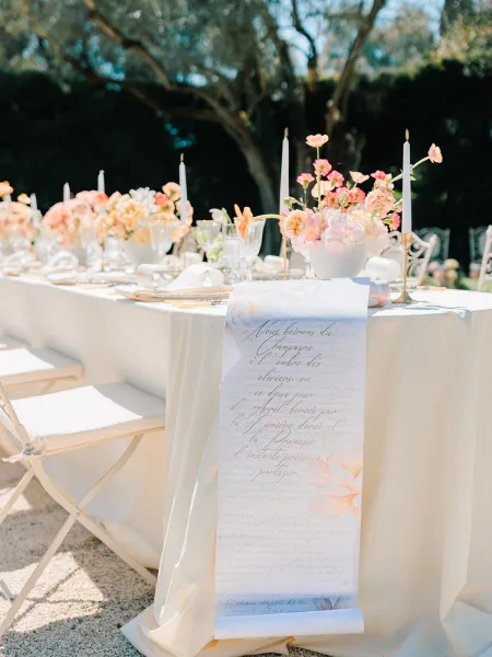 Reception tablescape with white linen tablecloth, pastel floral centerpieces and taper candles in brass candlesticks on a sunlit garden patio