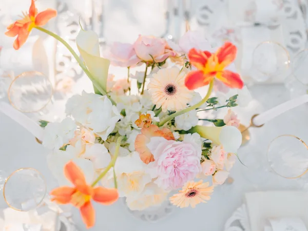Wedding centerpiece with a floral table centerpiece of calla lilies, blush and orange blooms, and taper candles on a white linen reception table