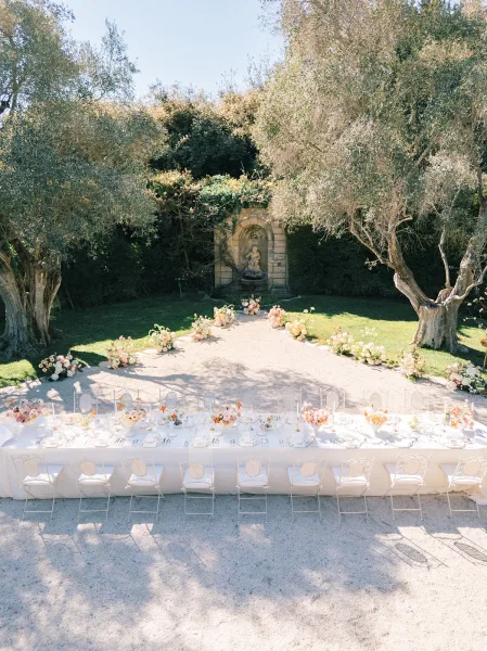 Reception tablescape for an outdoor wedding reception on a long banquet table with pastel florals, taper candles, and olive trees behind