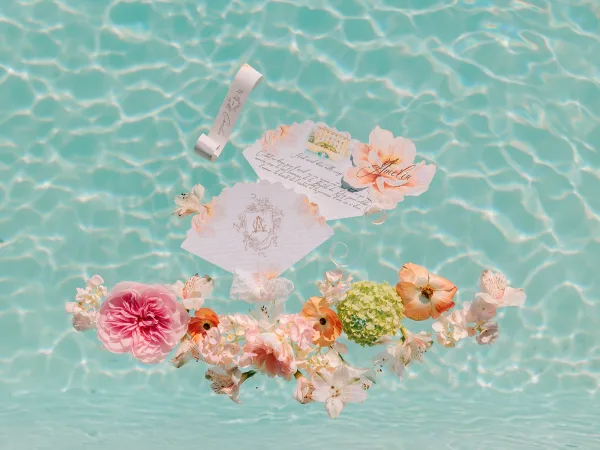 Wedding invitations floating on rippled pool water, a wedding invitation suite with handwritten calligraphy, ribbon and wax seal details