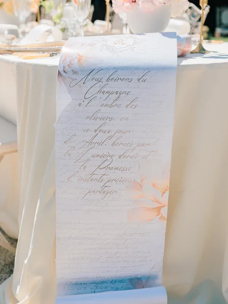 Wedding menu card with calligraphy wedding menu on watercolor paper at a place setting with gold flatware, wine glass, candle and greenery outdoors
