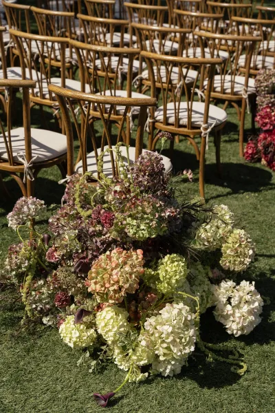Ceremony aisle decor with outdoor ceremony chairs, white cushions, and hydrangea-and-calla lily florals on a grass lawn