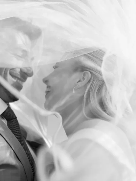 Wedding couple portrait of bride and groom close up under a bridal veil, laughing forehead to forehead, suit and tie in soft blurred light