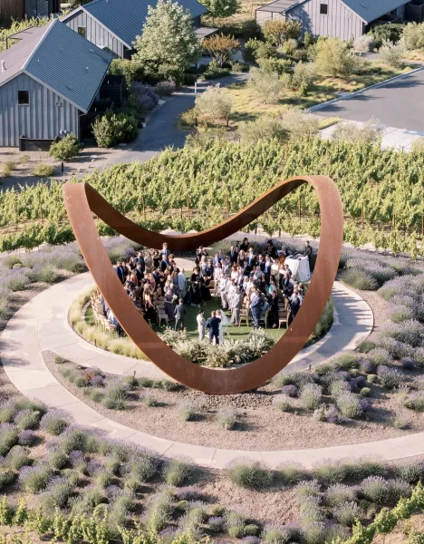 Outdoor wedding ceremony in a vineyard wedding ceremony with circular seating around a sculptural arch, lavender-lined aisle, and hillside backdrop