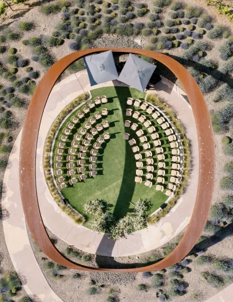 Ceremony setup with outdoor ceremony seating on green turf around a circular ring altar, with umbrellas and florals in desert gravel landscape