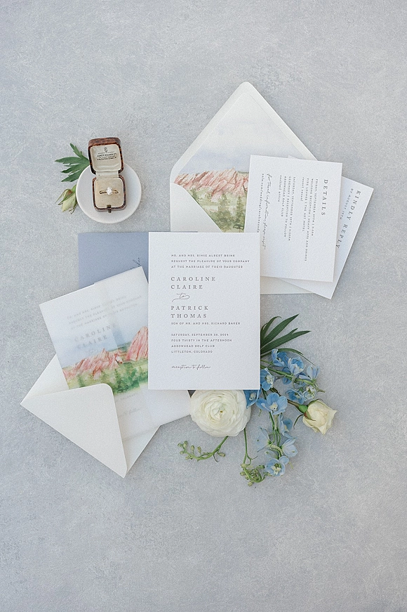 Wedding invitation suite with watercolor wedding invitation, RSVP and details cards, envelopes, and engagement ring on gray stone with blue flowers