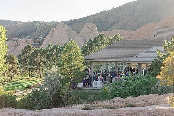 Wedding cocktail hour with guests mingling around linen cocktail tables and glassware on a string-lit terrace overlooking mountains and pines