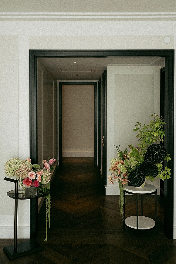 Wedding floral arrangement with wedding entry florals in a glass vase on pedestal tables, trailing amaranthus in an indoor hallway with black door frame
