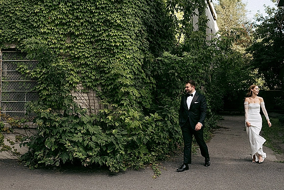 Wedding couple portrait of bride and groom walking, groom looking at bride by an ivy-covered wall, bride in strapless dress with opera gloves
