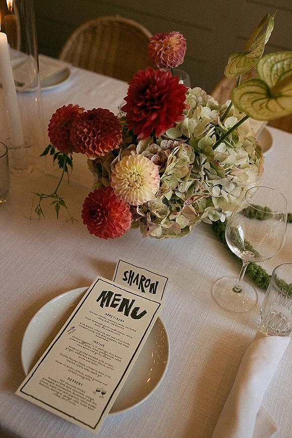 Reception tablescape with wedding table centerpiece of dahlias and hydrangea, menu and place cards, taper candles, and wood wall backdrop