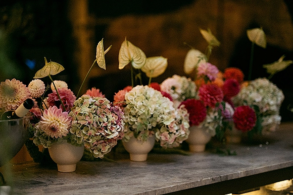 Wedding floral centerpieces with hydrangea centerpiece ideas in ceramic vases, dahlias and anthurium on a stone counter in warm ambient light