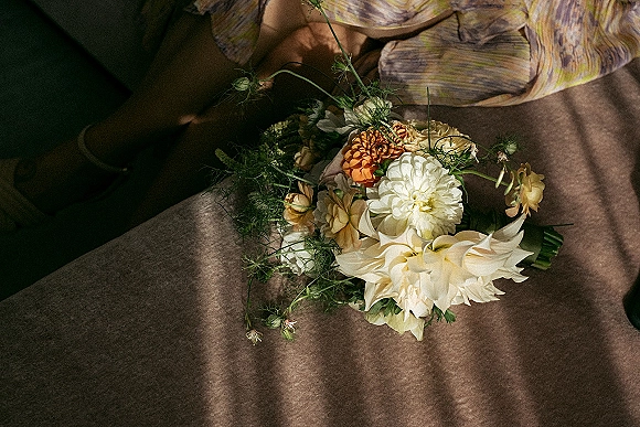 Bridal bouquet with dahlia wedding bouquet blooms, greenery, wildflower stems, and ribbon resting on a couch in soft window light