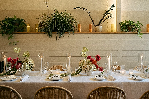 Reception tablescape with wedding head table decor, hydrangea and dahlia centerpieces, taper candles in hurricanes, and rattan chairs by shiplap wall