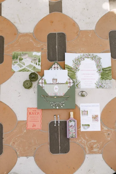 Wedding invitation suite featuring illustrated wedding invitations and a green envelope, arranged on a patterned terracotta tile floor.