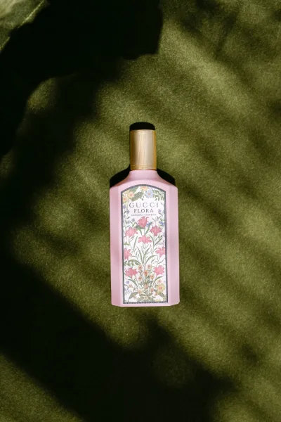 Perfume bottle, a wedding perfume with a floral label, set on green fabric with shadows across the background.