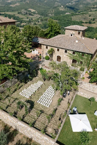 Ceremony setup with outdoor ceremony seating facing a floral ceremony arch in a stone villa courtyard, framed by trees and rolling hills.