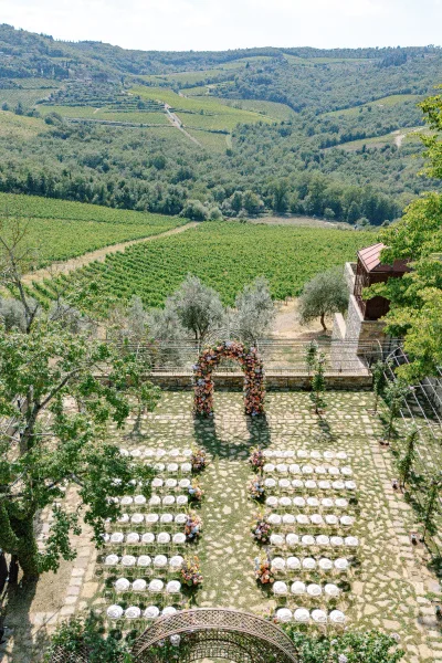 Ceremony setup for a vineyard ceremony featuring a floral arch on a stone terrace with rolling hills and trees beyond.