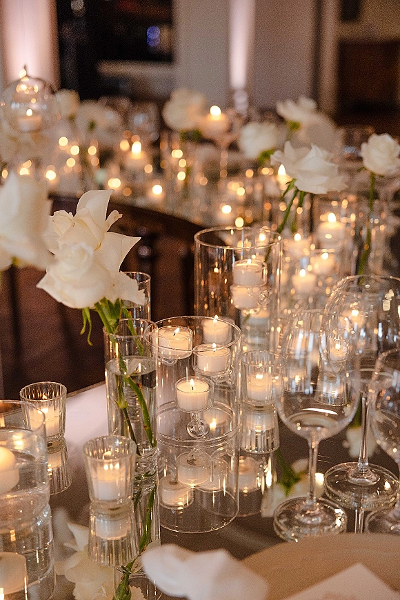 Candlelit wedding tablescape with wedding candle centerpiece of floating and votive candles in glass cylinders, accented by white roses and stemware