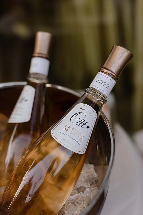 Wine bottle detail with rosé wine bottle label nestled in a metal ice bucket with ice on a tabletop against green drapery