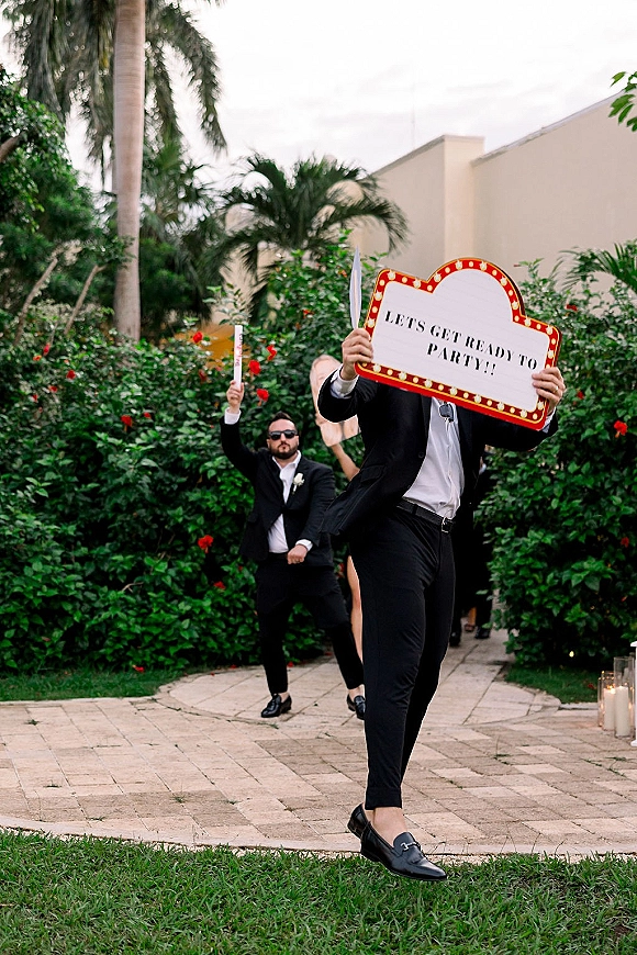 Wedding reception entrance with bridal party holding sparklers, framed by marquee and letter board signs along a candlelit stone walkway outdoors