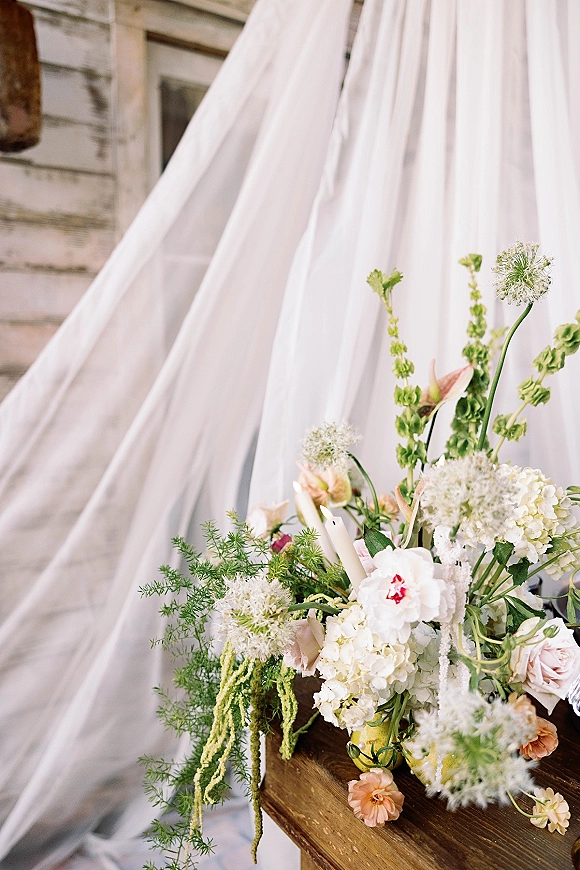 Wedding bouquet in a garden style bouquet of hydrangea, roses, and greenery on a wooden table with a white candle against a rustic wood wall