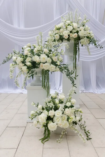 Ceremony flowers with white rose altar arrangements set against white drapery and a stone tile floor.