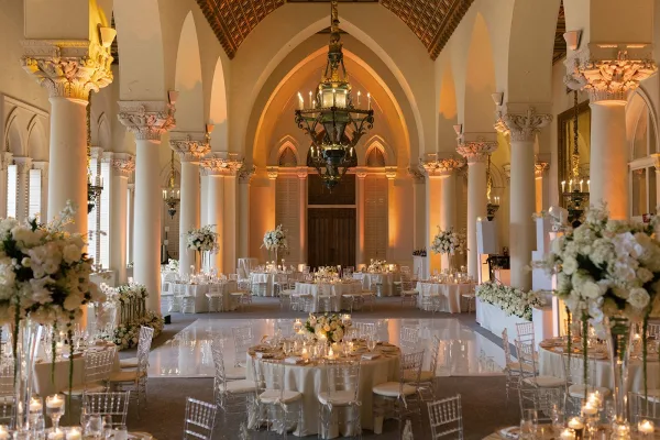 Reception decor for a ballroom wedding reception, featuring tall centerpieces in an arched hall with columns and a soaring vaulted ceiling.
