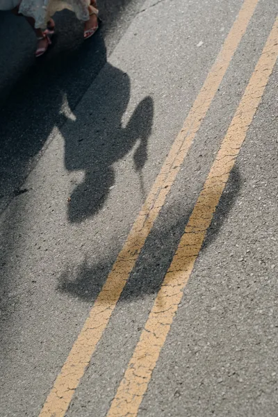 Couple shadow photo of bride and groom holding hands on a sunlit road with double yellow lines, dress hem and strappy heels visible