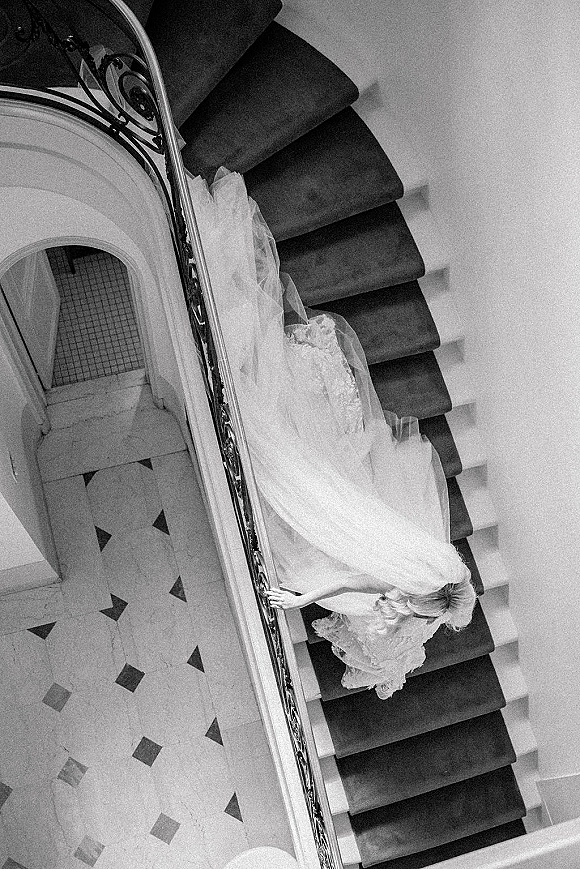 Bride portrait from above with a flowing tulle skirt and veil on a curved staircase with wrought iron railing and tiled floor