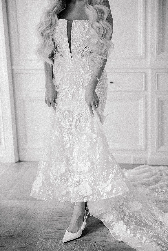 Wedding dress with a strapless lace bodice and plunge neckline, long train and pointed heels on a wooden floor by white paneled doors