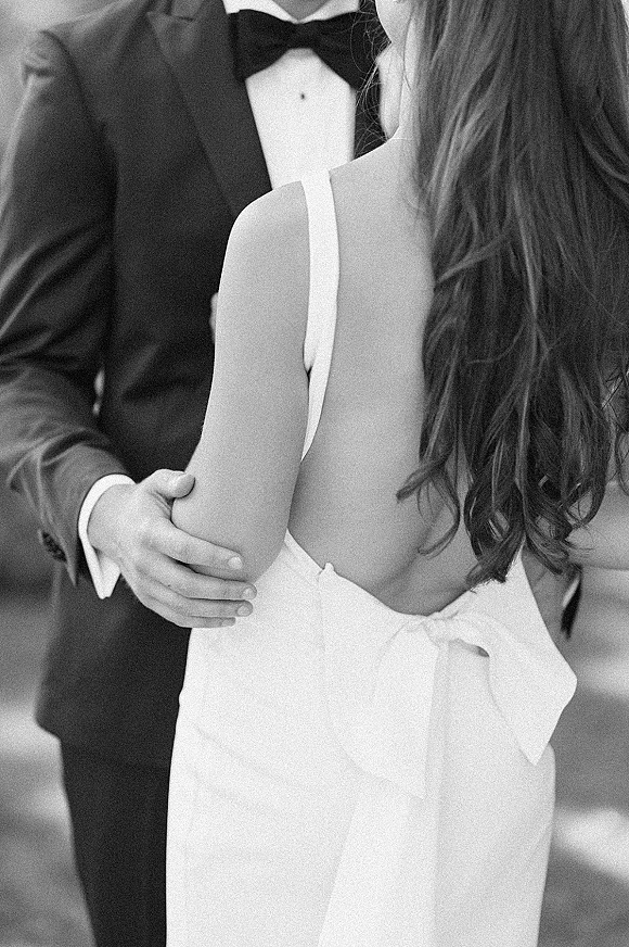 Couple portrait, black and white wedding portrait of bride and groom embracing in a slow dance, her strapless dress with bow detail, tuxedo and bow tie in blurred indoor setting