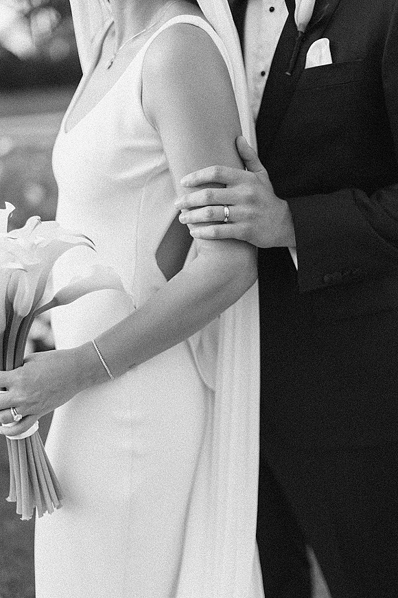 Couple portrait in a black and white wedding portrait style, bride with calla lily bouquet and veil beside groom in tuxedo, blurred foliage behind