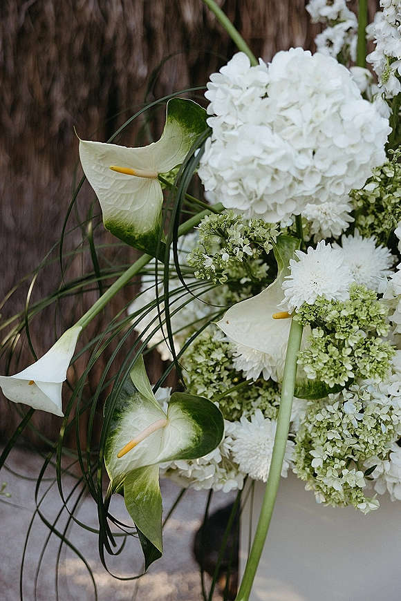 Wedding bouquet with calla lily bouquet accents, blending white hydrangea and greenery, set against a wooden fence by a stone walkway