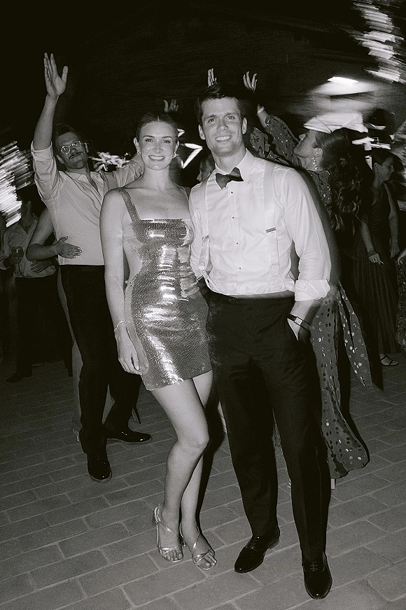 Wedding reception portrait in black and white of couple on a dance floor, bride in sequin mini dress as guests dance under string lights