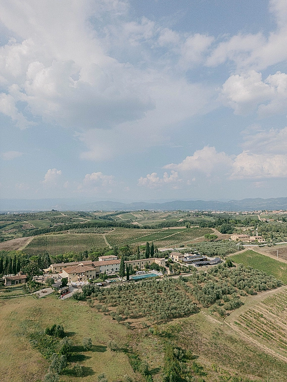 Wedding venue aerial view of a vineyard estate with a swimming pool, estate buildings, cypress trees, and rolling hills to distant mountains