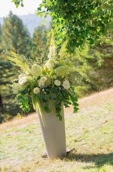 Ceremony floral arrangement in a tall vase with white calla lilies and hydrangeas, set in a sunlit meadow with forest and mountains