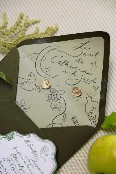 Wedding invitation suite with illustrated wedding invitations, black envelope and scalloped card, styled on striped linen with greenery and apple