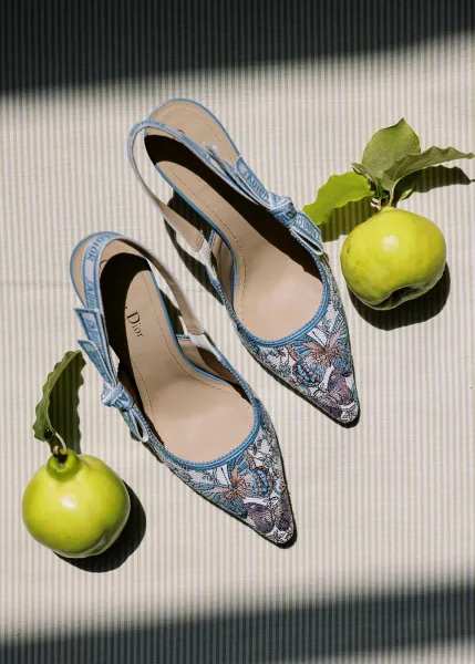 Bridal shoes in blue wedding shoes slingback style with butterfly embroidery, styled with apples and leaves on striped fabric in soft shadows