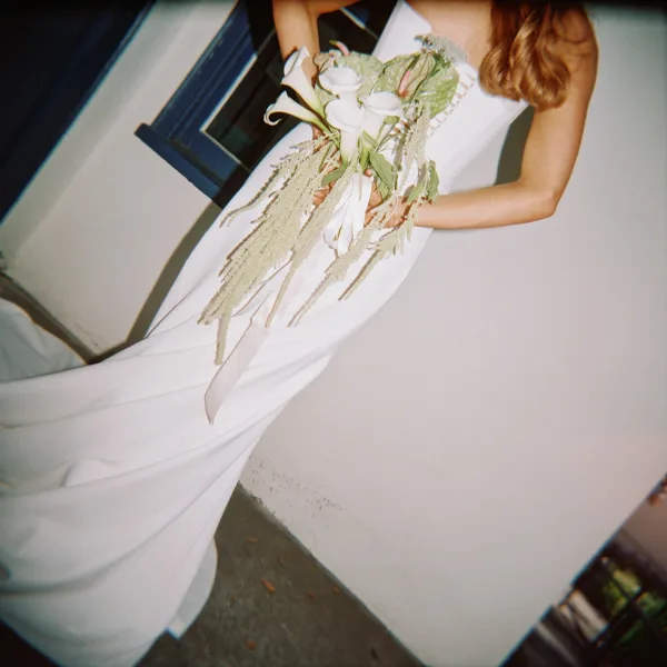 Bridal portrait of a bride holding bouquet with white calla lilies and cascading amaranthus, posing by a stucco wall and window