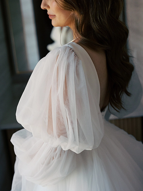 Wedding dress detail showing a puff sleeve wedding dress with sheer tulle overlay, square neckline and low back in soft window light indoors