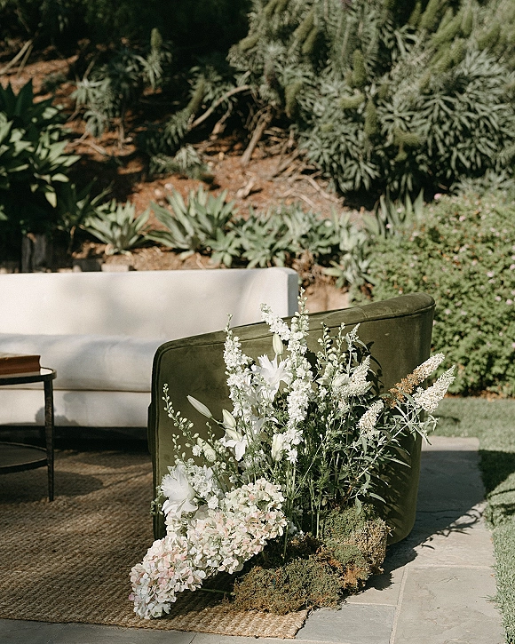 Wedding lounge seating with a green velvet sofa and white sofa beside a floral arrangement on a jute rug on a garden stone patio