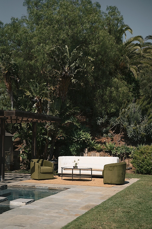 Lounge seating area with wedding lounge seating, featuring a white sofa and green chairs around a coffee table by the pool on a stone patio