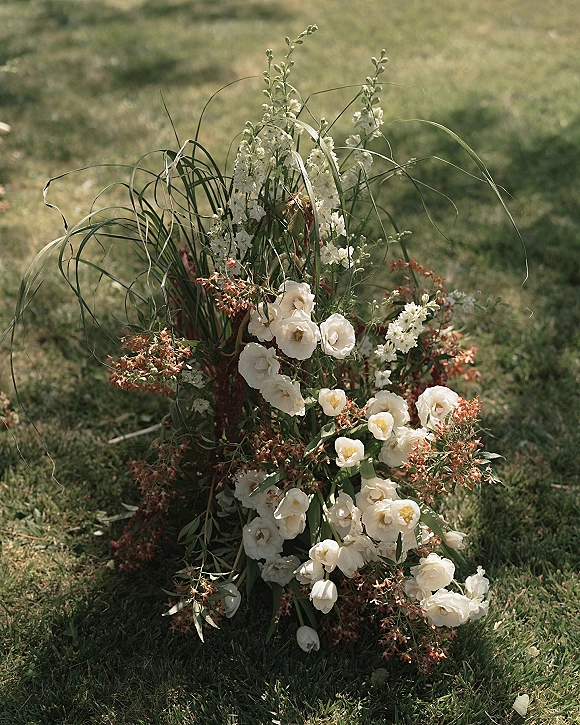 Wedding florals ground floral arrangement of white and red blooms with greenery and ornamental grass on a grass lawn in an outdoor field