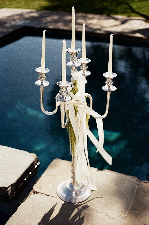 Wedding candelabra with silver candelabra decor, white taper candles, ribbon and greenery wrap set beside a pool on a stone deck