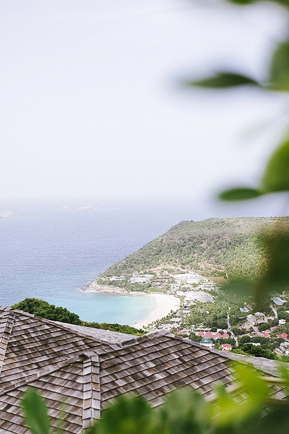 Beach wedding venue with a shingled roof overlooking an ocean bay, sandy beach, hillside village, tropical greenery, and sky