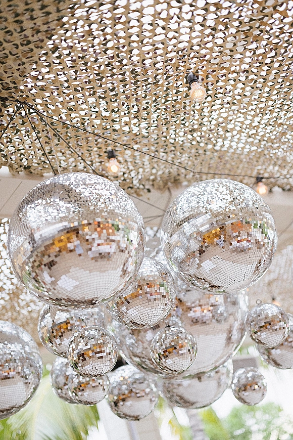 Disco ball decor with hanging disco balls and string lights beneath a camouflage net canopy under an outdoor tent ceiling with greenery