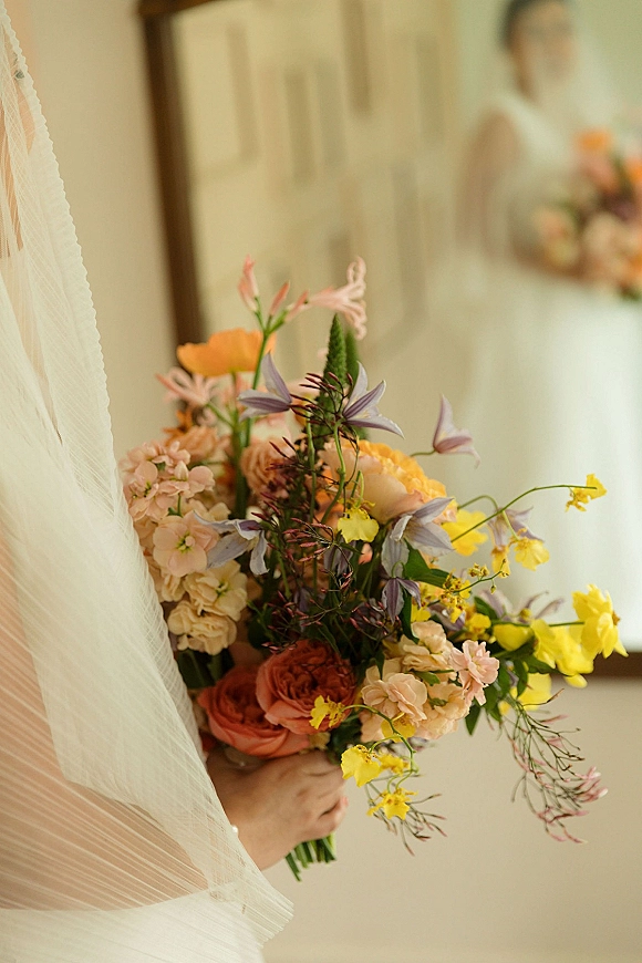 Bridal bouquet with a colorful bridal bouquet mix of bright blooms and greenery, framed by a soft veil with the bride blurred indoors